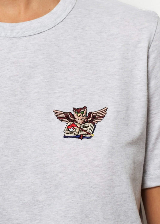 Femme avec un tee shirt gris brodé d'un hibou devant un palais